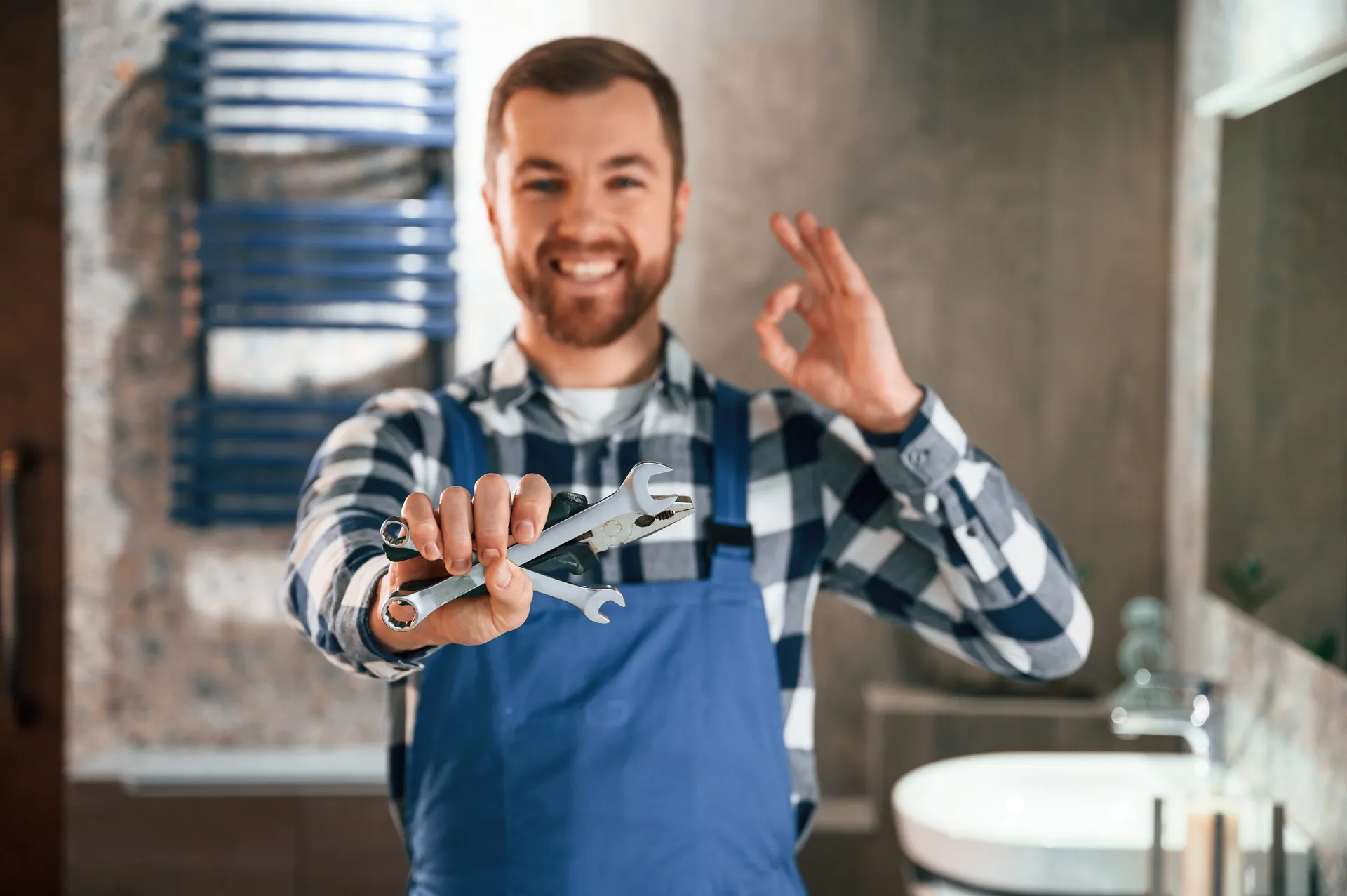 Smiling plumber holding wrenches in a modern bathroom
