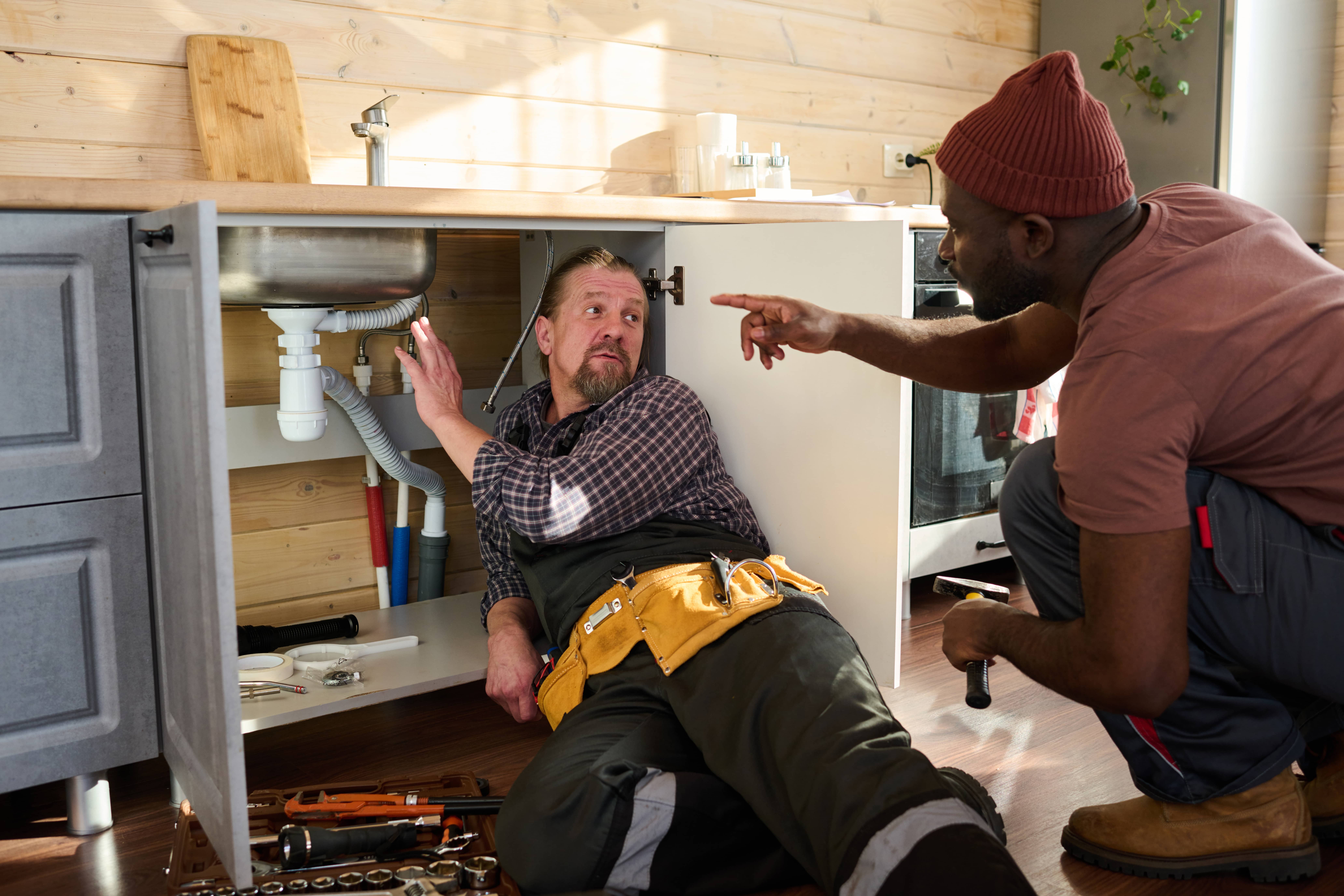 Plumbers explaining a repair under a kitchen sink
